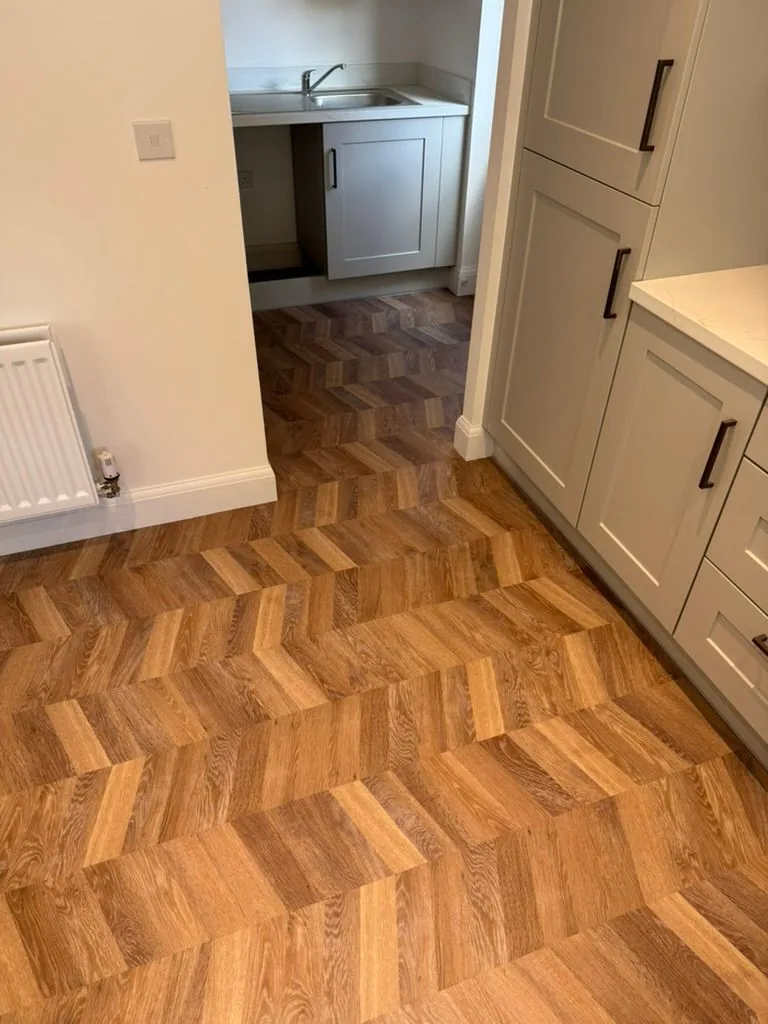 Chevron Karndean Knight Tile in warm oak across a kitchen and adjoining utility space with grey Shaker cabinets