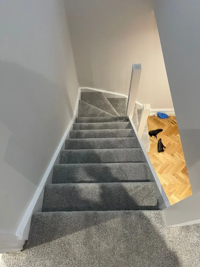 Overhead view of a straight flight carpeted in charcoal grey, meeting herringbone wood flooring at the base