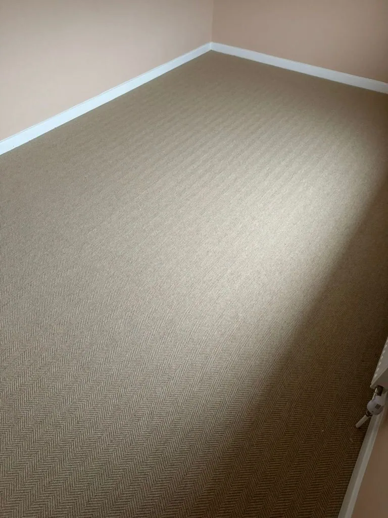 Natural-tone herringbone-weave carpet in a corner with peach walls and white skirting