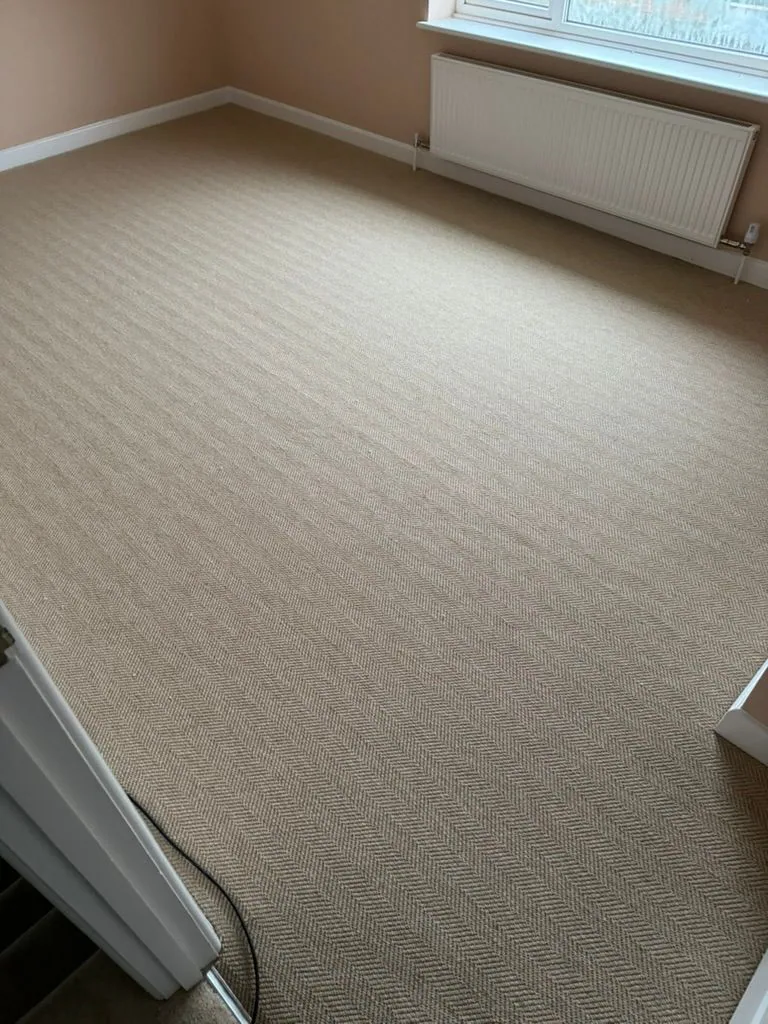Neutral herringbone carpet across a room with white trim and radiator under a window