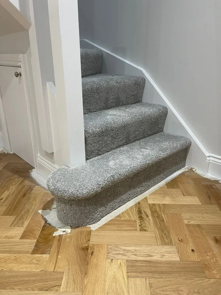 Grey textured stair carpet with bullnose tread meeting herringbone wood at the foot of the stairs