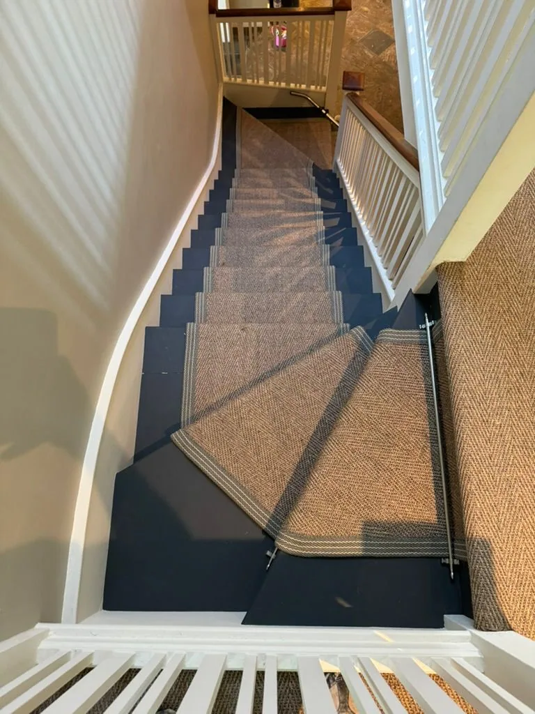 Winding staircase with tan herringbone sisal runner, striped binding and brushed aluminium stair rods
